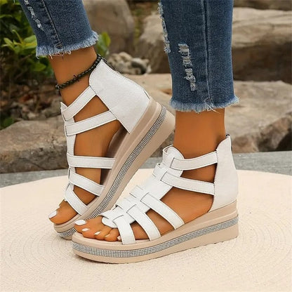 Weiße Sandalen mit Keilabsatz und Riemchen-Design, getragen von einer Person in zerrissenen Jeans. Modische Sommerschuhe für Damen.