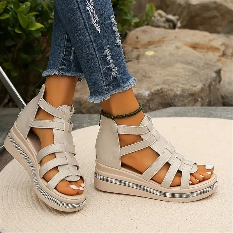 Beige Sandalen mit Keilabsatz und Riemchen-Design, getragen mit zerrissenen Jeans. Modische Damen-Sommerschuhe auf hellem Teppich.