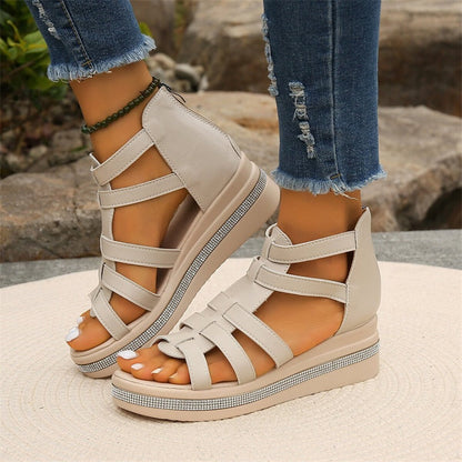 Beige Sandalen mit Keilabsatz und Riemchen, getragen von Person in zerrissenen Jeans. Modische Sommerschuhe, ideal für Freizeit und Strand.