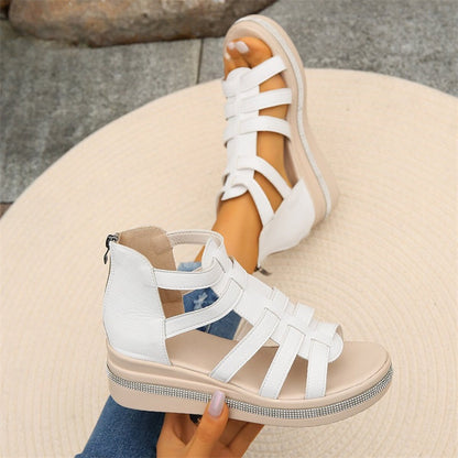 Weiße Sandalen mit Keilabsatz und Riemchen-Design, getragen von einer Person auf einem runden, beigen Teppich. Modische Sommerschuhe für Damen.