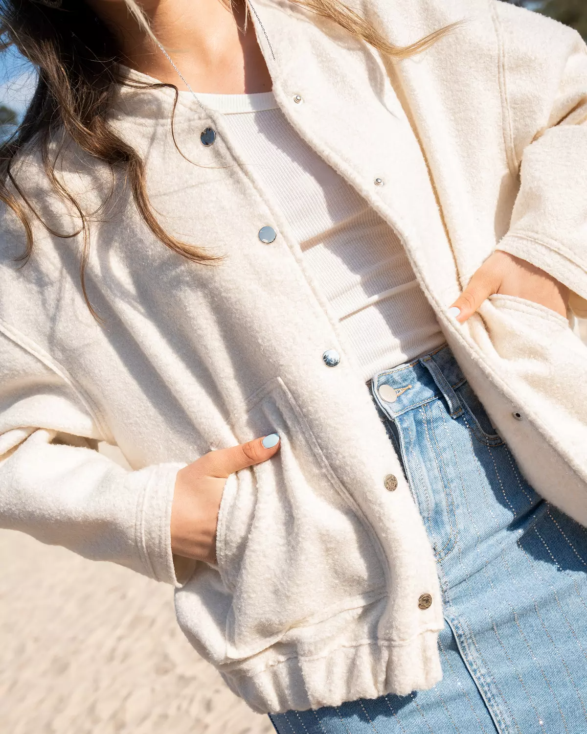Frau in weißer Strickjacke und Jeansrock am Strand, modischer Freizeitlook, Sommermode, stilvolle Damenbekleidung, Outdoor-Fashion.