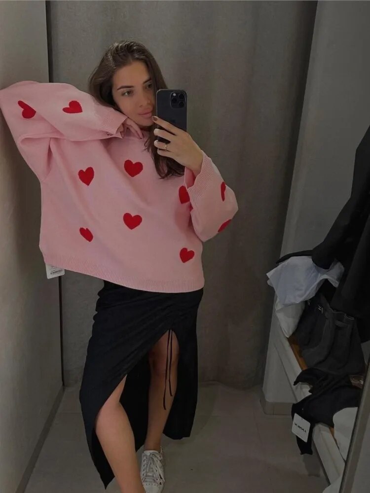 Frau im rosa Pullover mit roten Herzen, schwarzem Rock und weißen Sneakers macht Selfie im Spiegel. Modetrend, lässiger Look, Damenmode.