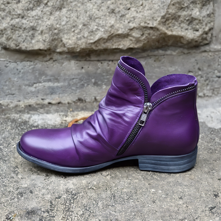 Lila Lederstiefel mit Reißverschluss, seitlich auf Betonboden vor Steinmauer. Modischer Damenstiefel, urbaner Stil, Herbstmode.