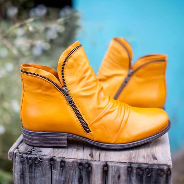 Orange Damenstiefeletten mit Reißverschluss, aus Leder, auf rustikalem Holztisch vor blauem Hintergrund. Modische Herbstschuhe, trendige Damenmode.