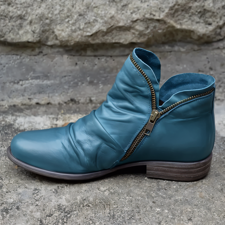 Blauer Lederstiefel mit seitlichem Reißverschluss, moderner Stil, auf Betonhintergrund. Hochwertige Damenmode, stilvolle Herbstschuhe.