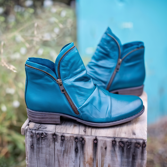 Türkise Lederstiefeletten mit Reißverschluss auf rustikalem Holzhocker, modische Damenstiefel, Herbstmode, stilvolle Schuhe, Outdoor-Hintergrund.