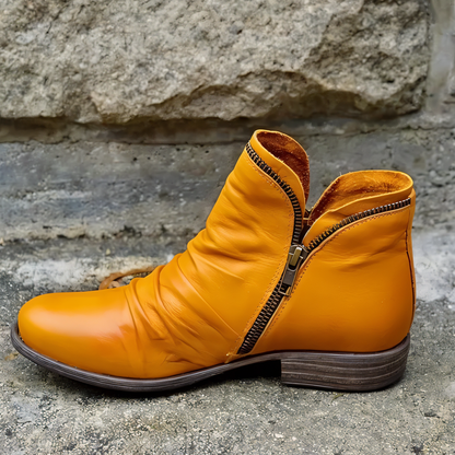 Orange Damenstiefelette mit Reißverschluss, aus Leder, auf grauem Steinboden. Modische Herbstschuhe, bequemer Absatz, trendiges Design.