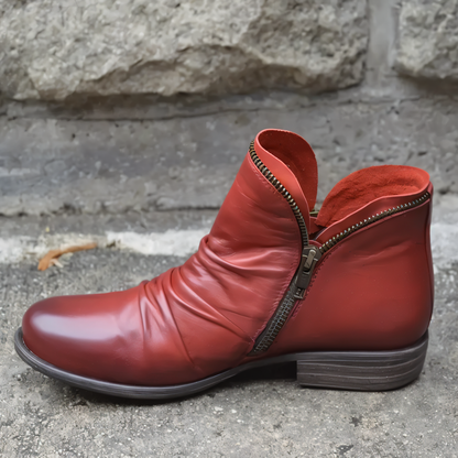 Roter Lederstiefel mit Reißverschluss, seitlich auf Betonboden vor Steinmauer. Modischer Damenstiefel, Herbstschuh, elegantes Design.