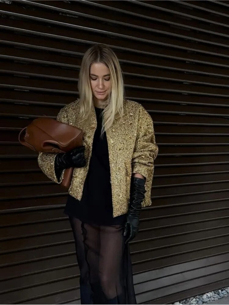 Frau in goldener Jacke und schwarzem Kleid, hält braune Tasche, trägt schwarze Handschuhe, vor dunklem Hintergrund. Fashion, Eleganz, Stil.