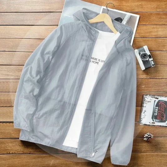 Graue Windjacke mit Kapuze auf Holztisch, daneben Kamera und Zeitschrift. Leichte, modische Jacke für Herren, ideal für Outdoor-Aktivitäten.