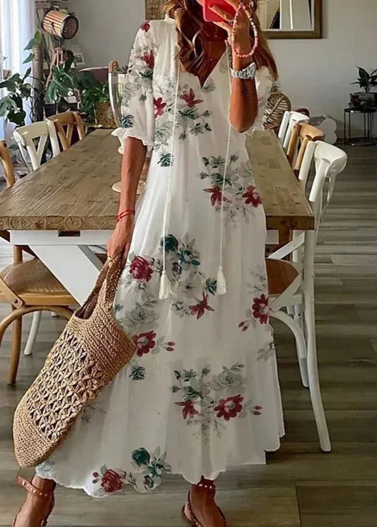 Frau in langem, geblümtem Sommerkleid mit Strohtasche steht in modernem Esszimmer. Mode, Sommerkleid, Blumenmuster, Strohtasche, Inneneinrichtung.