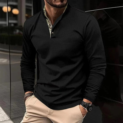 Mann in schwarzem Langarmhemd und beigen Hosen, steht vor einem modernen Gebäude. Stilvolle Herrenmode, elegantes Freizeitoutfit, urbane Kulisse.