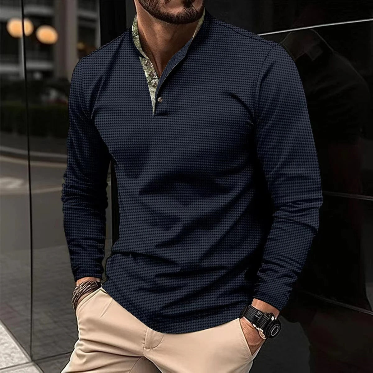 Mann in dunkelblauem Hemd mit Stehkragen und beiger Hose, steht auf städtischer Straße. Elegante Herrenmode, Freizeitlook, urbane Kulisse.