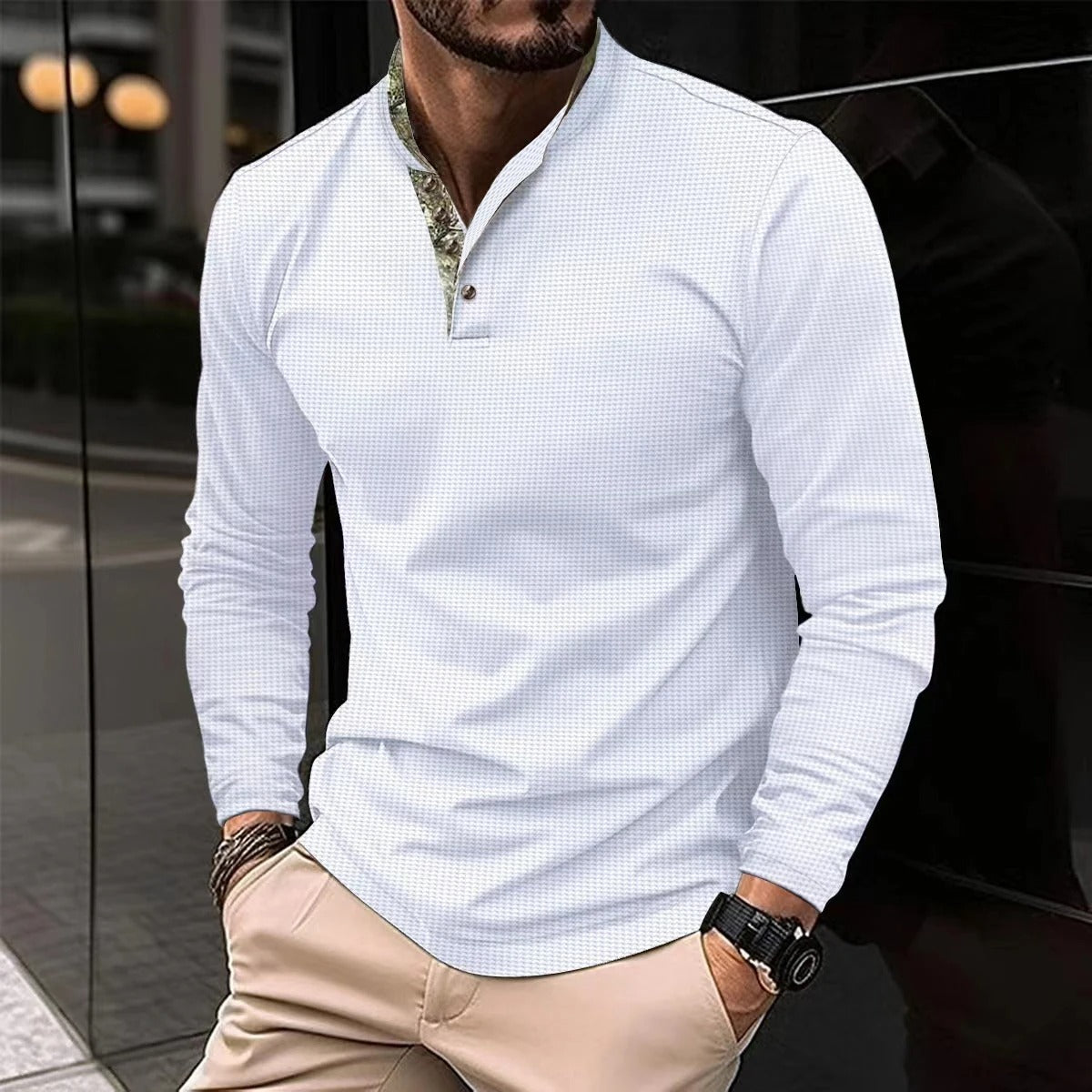 Mann in weißem, langärmligem Hemd mit Stehkragen und Knopfleiste, kombiniert mit beigen Hosen. Elegante Herrenmode, urbaner Stil.