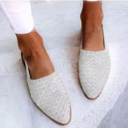 Damenfüße in weißen, geflochtenen Loafern auf grauem Boden. Modische Sommerschuhe, bequem und stilvoll, ideal für Freizeitkleidung.