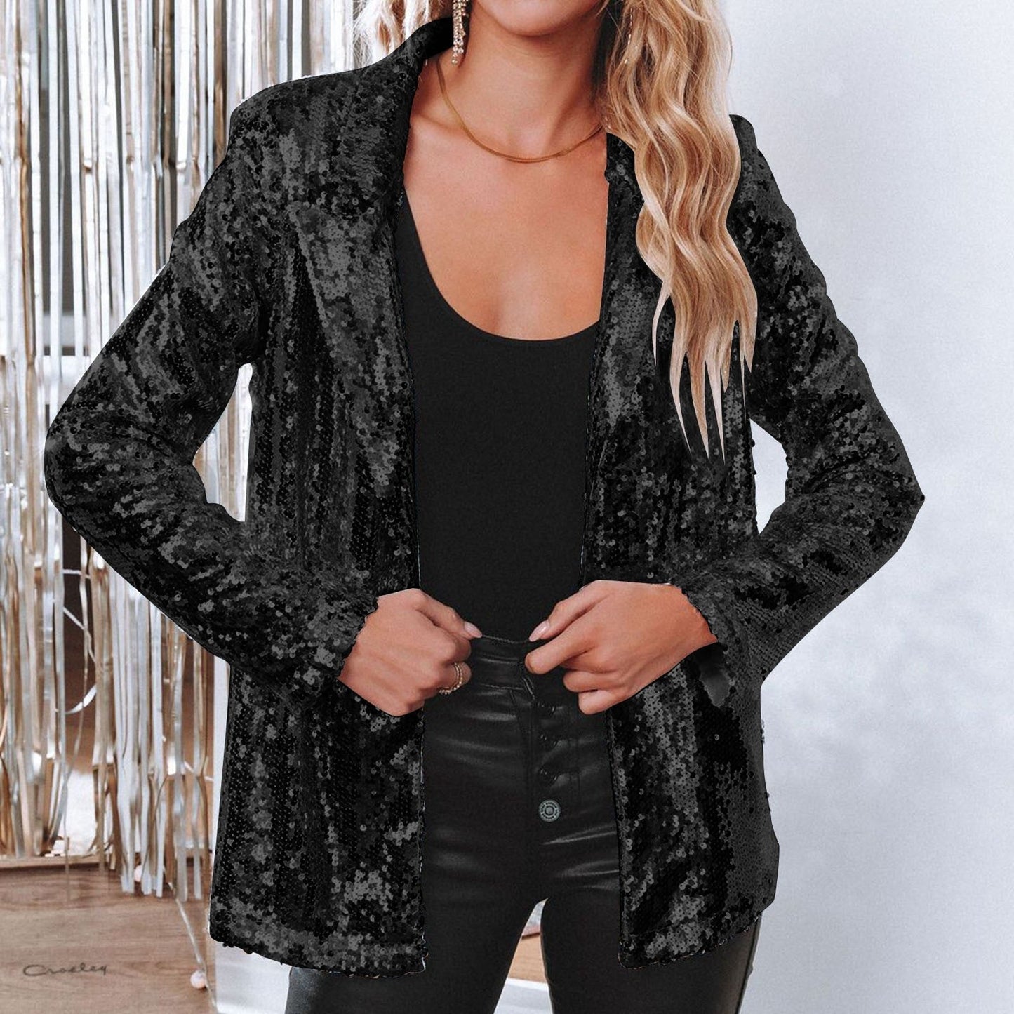 Frau in schwarzer Paillettenjacke, schwarzem Top und Lederhose vor silbernem Hintergrund. Elegante Mode, Abendgarderobe, stilvoller Look.