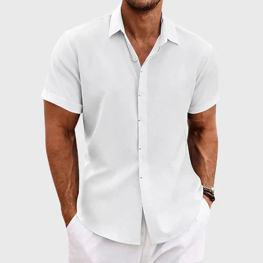 Mann in weißem, kurzärmligem Hemd und weißer Hose vor grauem Hintergrund. Sommermode, Herrenbekleidung, eleganter Freizeitlook.