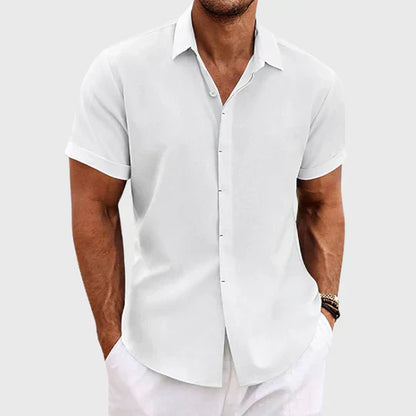 Mann in weißem, kurzärmligem Hemd und weißer Hose vor grauem Hintergrund. Sommermode, Herrenbekleidung, eleganter Freizeitlook.