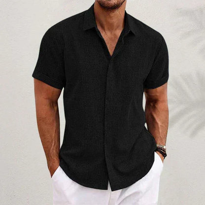Mann in schwarzem Kurzarmhemd und weißen Shorts vor neutralem Hintergrund. Sommermode, Herrenbekleidung, lässiger Stil.